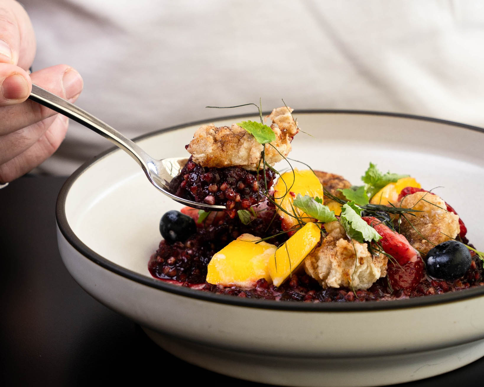 A plate of quinoa topped with fried chicken, mango, and various fruits, with a fork in hand ready to serve.